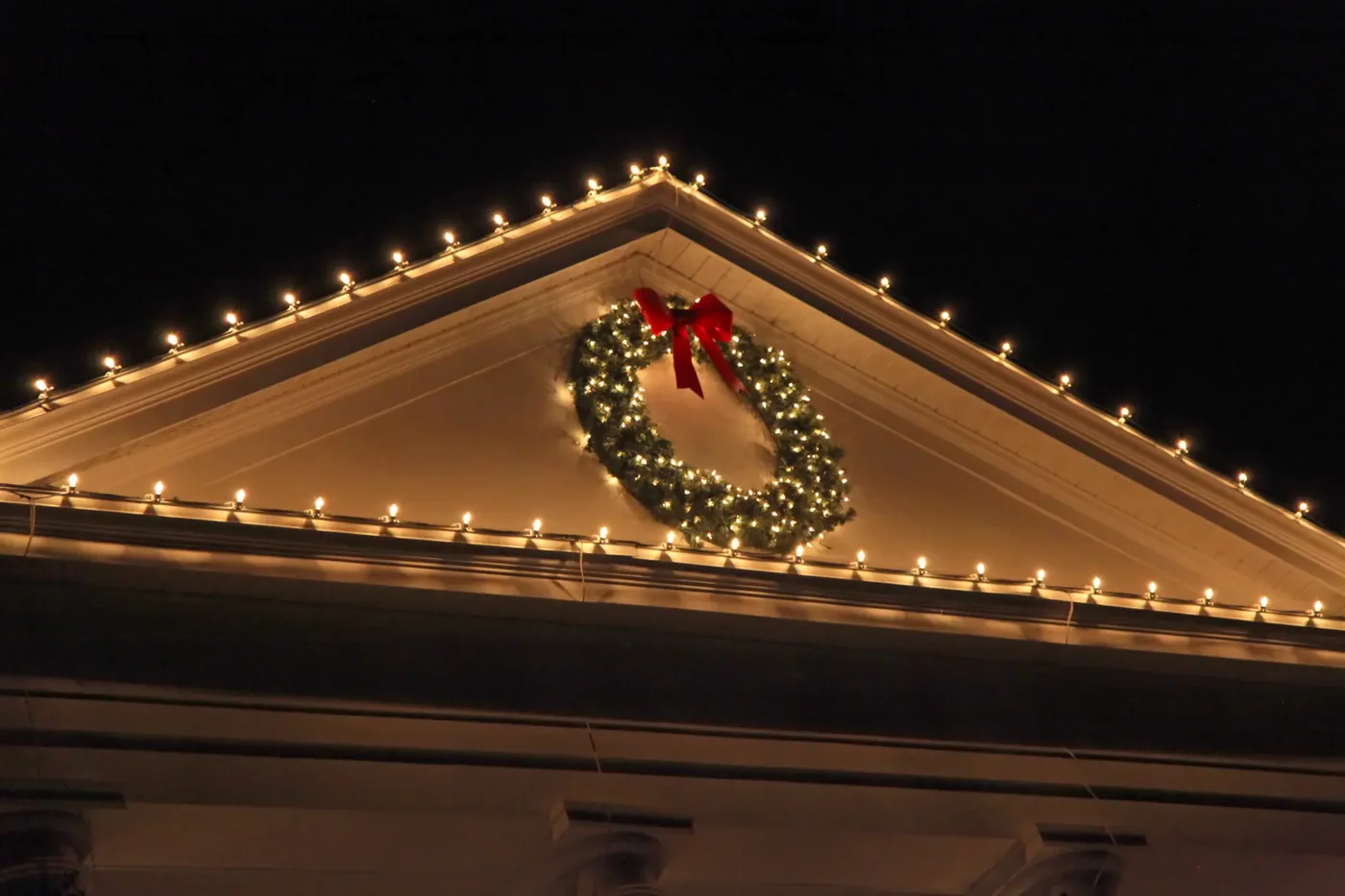 Warm white lights following a gable roofline around a Christmas wreath