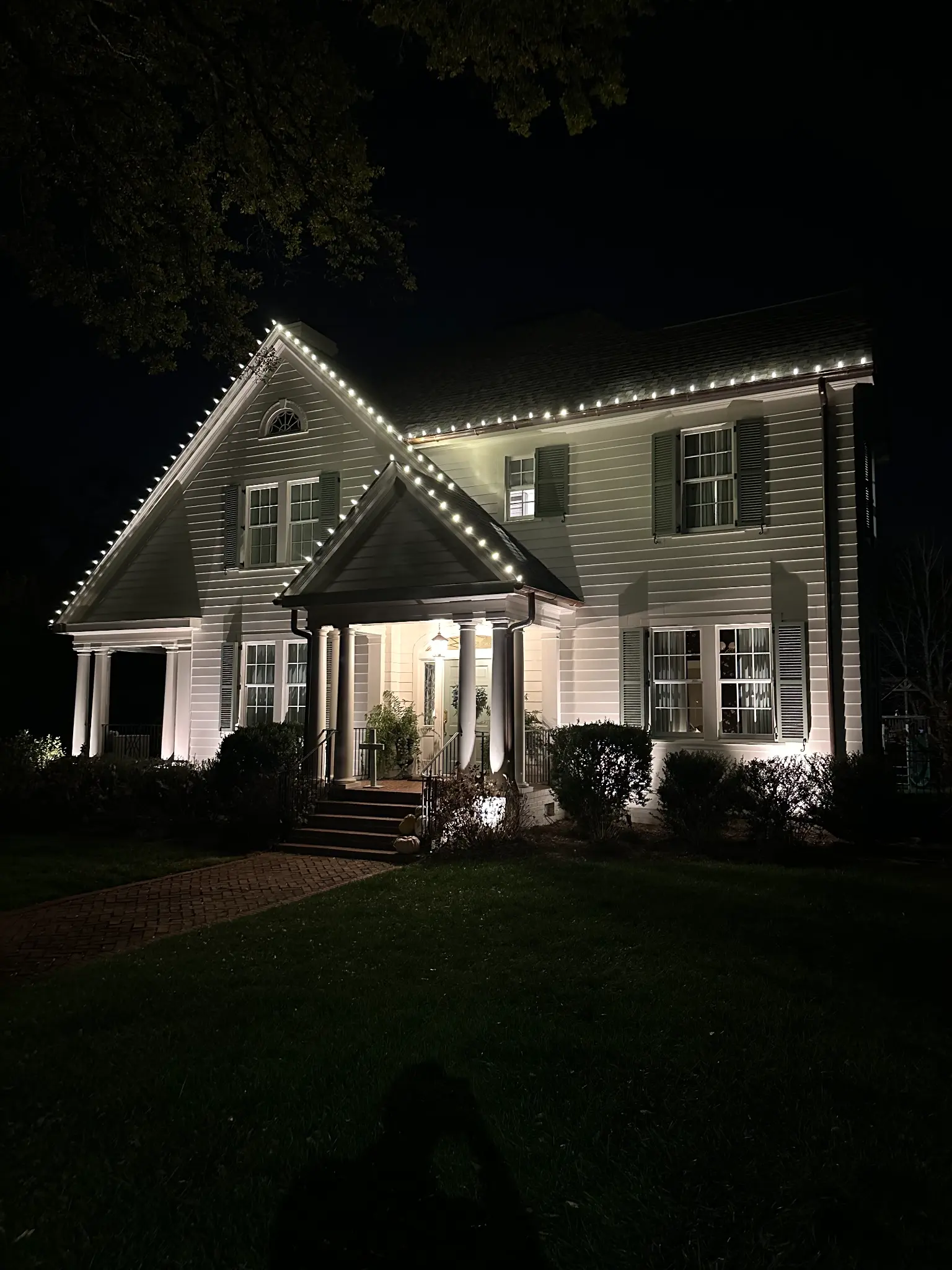 A real Tango Christmas Lights installation near Greenville, South Carolina: warm white bulbs following every roofline, the foundation shrubs netted in lights, and garland wrapped around the front porch columns